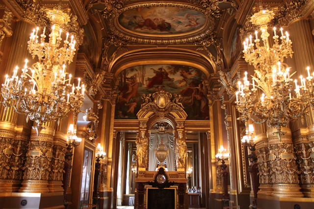 A grand, ornate hall with majestic chandeliers, intricate gold detailing, and elaborate wall and ceiling frescoes.